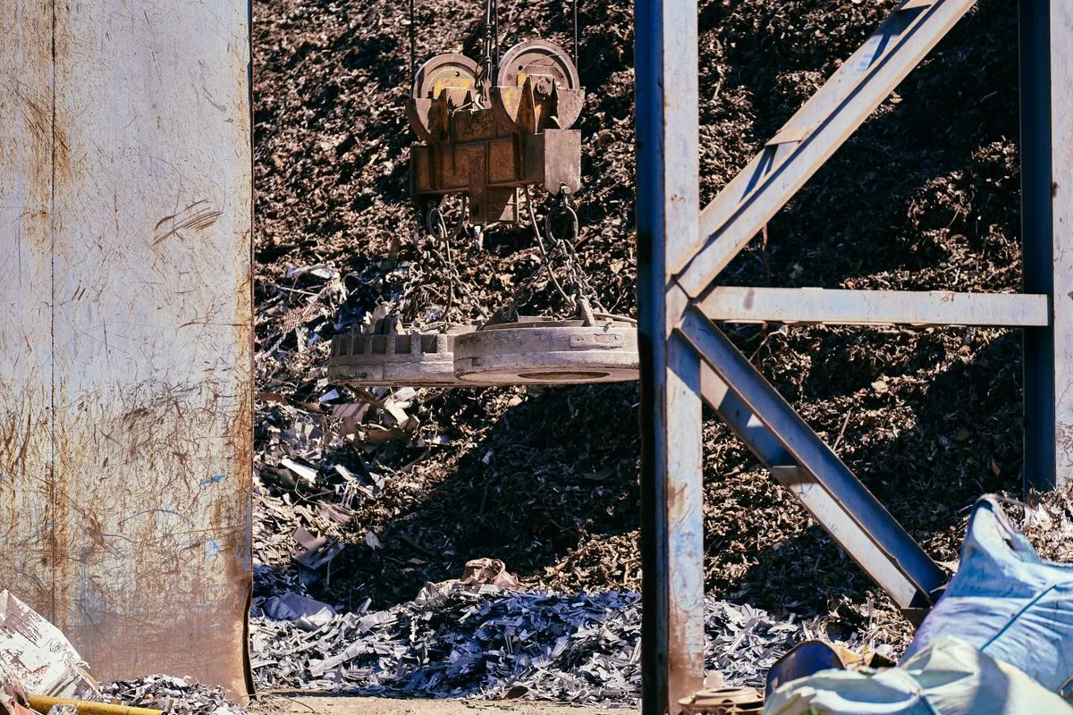Ímã industrial suspenso por corrente içando sucata metálica em pátio industrial